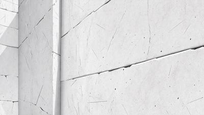 The primary subject of the image is a white wall with a pattern of holes in it. The setting is a room with a white wall, and the visual style is a close-up of the wall. The dominant colors are white and grey, creating a clean and minimalist atmosphere.