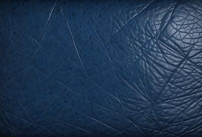 The primary subject of the image is a blue leather surface, which appears to be a leather-like material. The setting is a dark room, and the visual style is a close-up of the leather surface. The colors and mood of the image are dark and moody, with the blue leather providing a contrasting element.