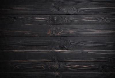 The primary subject of the image is a wooden wall with a black color. The setting is a room with a black wall, and the visual style is a close-up of the wooden wall. The colors and mood of the image are dark and moody, creating a sense of depth and texture.