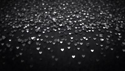 The primary subject of the image is a close-up of a black background with a pattern of hearts. The hearts are scattered across the background, creating a visually appealing and heartwarming scene. The setting is a black background, which provides a strong contrast to the hearts, making them stand out. The visual style of the image is a close-up, focusing on the hearts and their pattern. The colors and mood of the image are predominantly black, with the hearts adding a touch of warmth and positivity