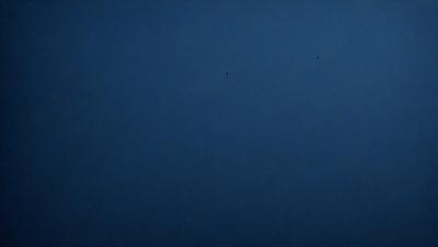 The primary subject of the image is the vast, dark blue sky. The setting is a clear, cloudless night, with no visible landmarks or objects. The visual style is a natural, unaltered photograph of the night sky. The colors and mood are predominantly dark and serene, with the blue hue creating a sense of calmness and tranquility.