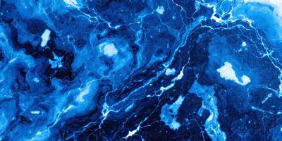 The primary subject of the image is a blue marble-like surface with a pattern of white streaks. The setting is a dark blue background, which contrasts with the white streaks. The visual style appears to be a combination of a photo and digital art, as the blue marble-like surface has a textured and detailed appearance. The colors and mood of the image are predominantly dark and moody, with the blue marble-like surface and white streaks creating a striking contrast against the dark blue background.