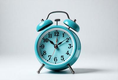 The primary subject of the image is a blue alarm clock with a white face. The clock is placed on a white surface, which serves as the background. The visual style of the image is a photo, capturing the alarm clock in its natural setting. The colors and mood of the image are predominantly white and blue, creating a clean and soothing atmosphere.