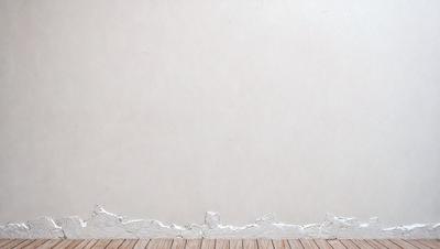The primary subject of the image is a white wall with a few small holes in it. The setting is a room with a wooden floor. The visual style is a photo, and the dominant colors are white and beige. The overall atmosphere is clean and minimalistic.
