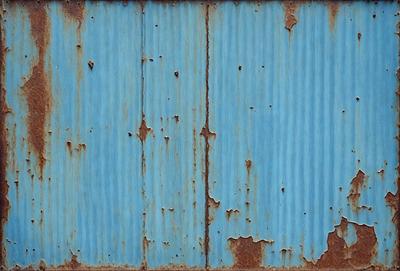 The primary subject of the image is a blue wall with rust and peeling paint. The setting is a room with a blue wall, and the visual style is a photo. The dominant colors are blue and rust, creating a mood of aging and deterioration.