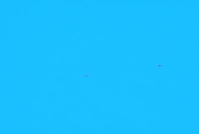 The primary subject of the image is a blue sky with two airplanes flying through it. The setting is a clear day with no clouds, providing a perfect backdrop for the airplanes. The visual style is a realistic representation of the scene, capturing the airplanes in flight. The colors and mood of the image are predominantly blue, creating a calm and serene atmosphere.
