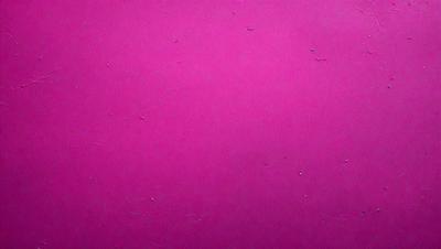 The primary subject of the image is a close-up of a pink surface, which appears to be a wall or a piece of fabric. The setting is indoors, and the visual style is a close-up, which emphasizes the pink color and texture of the surface. The colors and mood of the image are predominantly pink, creating a warm and inviting atmosphere.