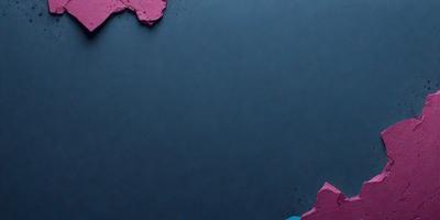The primary subject of the image is a blue background with a few pink and purple chips of paint on it. The setting appears to be a dark room, and the visual style is a close-up of the paint chips on the blue surface. The colors and mood of the image are predominantly dark and moody, with the pink and purple chips adding a touch of color to the otherwise monochromatic scene.