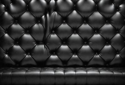The primary subject of the image is a black leather couch with a black and white pattern. The setting is a room with a black background, and the visual style is a close-up of the couch. The colors and mood of the image are predominantly black, giving it a sleek and modern appearance.