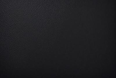 The primary subject of the image is a black leather surface. The setting is a black background, which creates a contrast with the leather. The visual style is a close-up of the leather, showcasing its texture and details. The colors and mood of the image are predominantly dark, with the black leather and background creating a moody atmosphere.