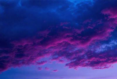The primary subject of the image is a purple cloudy sky. The setting is a cloudy day with a purple hue, creating a dramatic and moody atmosphere. The visual style is a natural, outdoor scene with no indication of being a photo, digital art, illustration, drawing, pattern, texture, or clipart. The colors and mood of the image are predominantly purple, with the cloudy sky adding a sense of depth and intensity to the scene.