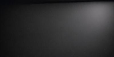 The primary subject of the image is a black background with a white light source. The setting is a dark room, and the visual style is a black and white photo. The colors and mood of the image are predominantly dark and moody, with the white light source creating a stark contrast against the black background.
