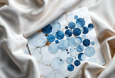 The primary subject of the image is a piece of artwork featuring a blue and gold design. The setting is a white cloth, which serves as the background for the artwork. The visual style appears to be a combination of digital art and illustration, creating a unique and eye-catching design. The dominant colors in the image are blue and gold, giving the artwork a sophisticated and elegant appearance.