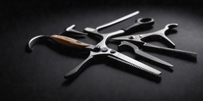 The primary subject of the image is a pair of scissors. The scissors are placed on a black surface, which serves as the setting or background. The visual style of the image is a photo, capturing the details of the scissors. The colors and mood of the image are dark and moody, with the black surface and the scissors' metal components creating a sense of depth and contrast.