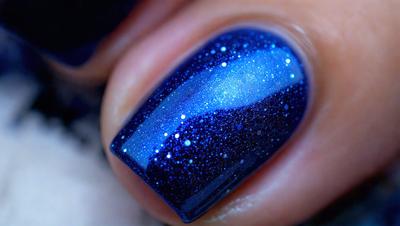 The primary subject of the image is a person's fingernail with a blue nail polish. The setting is a close-up of the person's fingernail, and the visual style is a photo. The dominant colors are blue and black, creating a calm and soothing atmosphere.