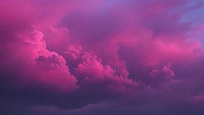 The primary subject of the image is a cloudy sky with pink and purple hues. The setting is a cloudy sky, and the visual style is a photo. The colors and mood of the image are predominantly pink and purple, creating a serene and calming atmosphere.