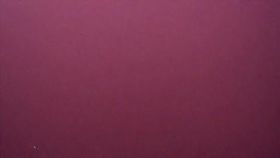 The primary subject of the image is a large, red surface. The setting appears to be a dark room, with the red surface being the main focus. The visual style of the image is a close-up of the red surface, which gives it a bold and striking appearance. The colors and mood of the image are predominantly red, creating a sense of intensity and vibrancy.