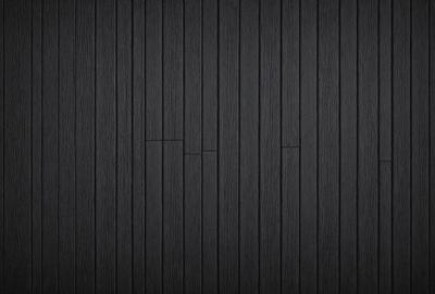 The primary subject of the image is a wooden wall. The setting is a black background, which creates a striking contrast with the wooden surface. The visual style is a close-up of the wooden wall, showcasing its texture and details. The colors and mood of the image are predominantly black, giving it a bold and dramatic appearance.