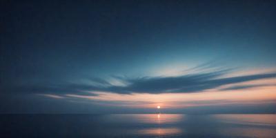 The primary subject of the image is a beautiful sunset over the ocean. The setting is a vast body of water with a cloudy sky above. The visual style of the image is a photo, capturing the stunning colors and atmosphere of the sunset. The colors and mood of the image are predominantly warm and serene, with the sun setting over the water, creating a peaceful and picturesque scene.