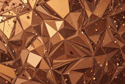 The primary subject of the image is a close-up of a brown and gold patterned surface, which appears to be a piece of art or a textured wall. The setting is indoors, with the patterned surface being the main focus of the image. The visual style is a combination of photo and digital art, creating a unique and intricate design. The colors and mood of the image are warm and inviting, with the brown and gold tones evoking a sense of richness and depth.