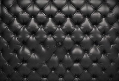 The primary subject of the image is a black leather couch with a patterned design. The setting is a room with a black background, and the visual style is a close-up of the couch. The colors and mood of the image are dark and moody, with the black leather couch being the main focus.