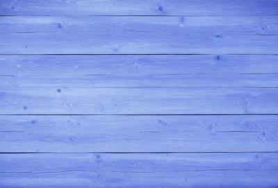 The primary subject of the image is a wooden wall with a blue color. The setting is a room with a blue wooden floor. The visual style is a close-up of the wooden wall, giving a sense of depth and texture. The colors and mood of the image are predominantly blue, creating a calm and serene atmosphere.