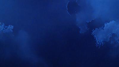 The primary subject of the image is a cloudy blue sky. The setting is a dark blue background, which creates a contrasting effect with the cloudy sky. The visual style is a photo, capturing the beauty of the cloudy sky. The colors and mood of the image are predominantly dark and moody, with the blue sky and clouds creating a dramatic atmosphere.