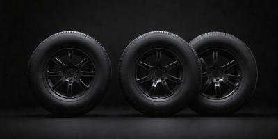 The primary subject of the image is a set of four black tires. They are placed on a black background, which creates a striking contrast with the tires. The visual style of the image is a photo, showcasing the tires in their natural setting. The colors and mood of the image are dark and dramatic, emphasizing the tires' shape and design.