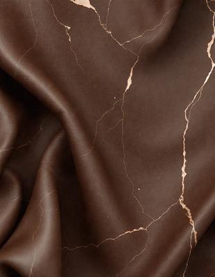 The primary subject of the image is a piece of brown leather, possibly a leather jacket or a leather material. The setting is a close-up of the leather, showcasing its texture and appearance. The visual style is a close-up, focusing on the details of the leather. The colors and mood of the image are predominantly brown, giving it a warm and natural feel.