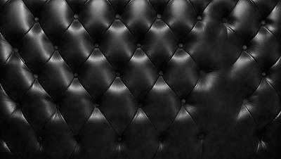 The primary subject of the image is a black leather couch with a black and white pattern. The setting is a room with a black background, and the visual style is a close-up of the couch. The colors and mood of the image are predominantly black, giving it a sleek and modern appearance.