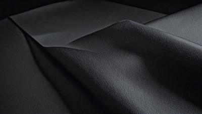 The primary subject of the image is a piece of fabric, which is the main object, scene, or focus of the image. The setting/background consists of a dark surface, possibly a table or a floor. The visual style of the image is a photo, as it captures the fabric's texture and details. The colors and mood of the image are predominantly dark, with the fabric being the main source of light and contrast.