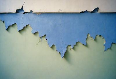 The primary subject of the image is a blue wall with peeling paint. The setting is a room with a green wall, and the visual style is a photo. The dominant colors are blue and green, creating a mood of decay and deterioration.