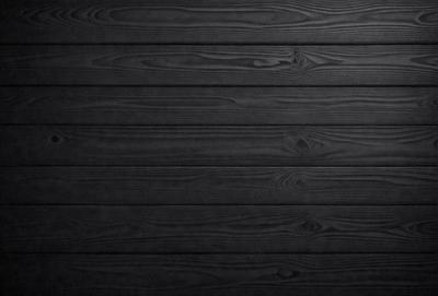 The primary subject of the image is a wooden wall. The setting is a dark room, and the visual style is a black and white photo. The colors and mood of the image are predominantly dark, creating a moody atmosphere.