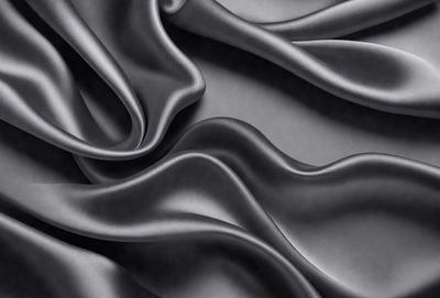 The primary subject of the image is a close-up of a black fabric, possibly a piece of silk or velvet. The setting is a dark background, which emphasizes the fabric's texture and color. The visual style is a close-up, focusing on the details of the fabric. The colors and mood of the image are predominantly dark, with the black fabric being the main focus.