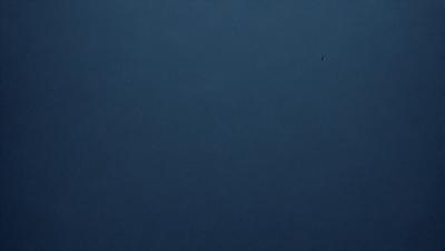 The primary subject of the image is a dark blue sky with no clouds. The setting is a vast, open space with no visible landmarks or objects. The visual style is a simple, unadorned representation of the sky. The colors and mood are predominantly dark and moody, with the blue sky serving as the main focal point.