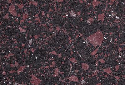 The primary subject of the image is a close-up of a marble surface with a red hue. The setting is a rocky surface, possibly a wall or a countertop. The visual style is a close-up of the marble, showcasing its texture and color. The dominant colors are red and black, creating a bold and striking appearance.