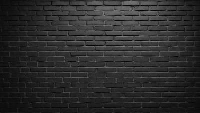 The primary subject of the image is a brick wall. The setting is a dark room, and the visual style is a black and white photo. The dominant colors are black and white, creating a moody atmosphere.