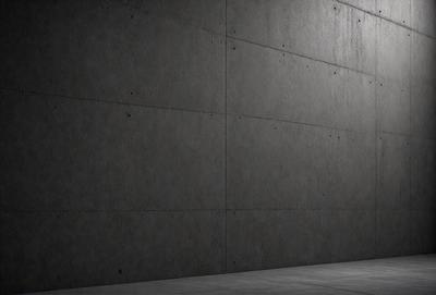 The primary subject of the image is a large concrete wall. The setting is a dark room, and the visual style is a black and white photo. The dominant colors are shades of gray, and the overall atmosphere is moody and dramatic.