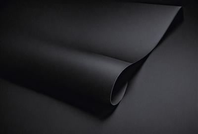The primary subject of the image is a black roll of fabric. The setting is a dark background, which emphasizes the fabric's color. The visual style is a close-up of the fabric, showcasing its texture and details. The colors and mood of the image are predominantly dark, with the black fabric being the main focus.