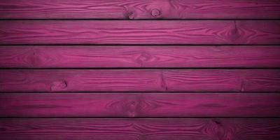 The primary subject of the image is a wooden wall with a pinkish hue. The setting is a room with a wooden floor. The visual style is a close-up of the wooden wall, showcasing its texture and color. The dominant colors are pink and brown, creating a warm and inviting atmosphere.