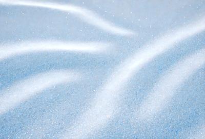 The primary subject of the image is a blue surface, possibly a piece of fabric or a wall, with a pattern of glittering blue and white swirls. The setting appears to be a beach, as the blue surface is located near the water. The visual style of the image is a combination of photo and digital art, creating a unique and eye-catching pattern. The colors and mood of the image are predominantly blue and white, giving it a calming and serene atmosphere.