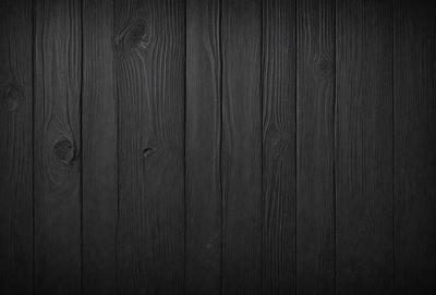 The primary subject of the image is a wooden wall. The setting is a dark room, and the visual style is a black and white photo. The colors and mood of the image are predominantly dark and moody, with the wooden wall being the main focus.