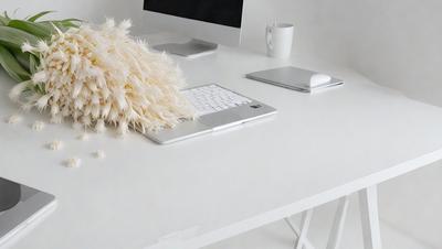 The primary subject of the image is a white desk with a laptop computer and a keyboard on it. The setting is an office environment, with a white desk and a computer. The visual style is a photo, and the colors and mood are predominantly white, giving the scene a clean and minimalist appearance.