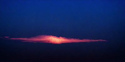 The primary subject of the image is a cloud, which is the main object, scene, or focus of the image. The cloud is set against a dark blue sky, creating a dramatic and moody atmosphere. The visual style of the image is a photo, capturing the cloud's shape and texture in detail. The colors and mood of the image are dominated by the dark blue sky and the cloud, which together evoke a sense of mystery and beauty.