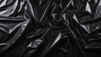 The primary subject of the image is a close-up of a black leather material, possibly a piece of fabric or a leather jacket. The setting is a dark background, which emphasizes the leather material. The visual style is a close-up, focusing on the details of the leather. The colors and mood of the image are predominantly dark, with the black leather material being the main focus.