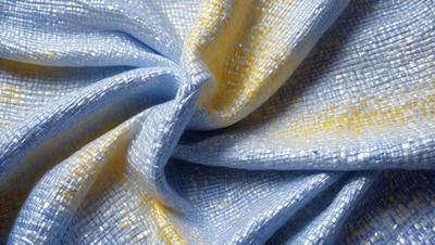 The primary subject of the image is a blue and yellow fabric, which is the main object, scene, or focus of the image. The setting is a close-up view of the fabric, showcasing its intricate design and texture. The visual style is a detailed, up-close representation of the fabric, which gives the image a realistic and artistic appearance. The dominant colors in the image are blue and yellow, creating a vibrant and lively atmosphere.