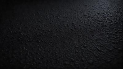The primary subject of the image is a black surface with water droplets on it. The setting is a dark room, and the visual style is a close-up of the black surface. The colors and mood of the image are predominantly dark and moody, with the water droplets adding a touch of wetness to the overall atmosphere.