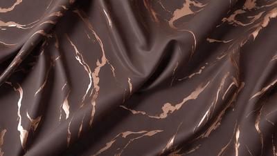 The primary subject of the image is a brown fabric with a gold pattern. The setting is a close-up view of the fabric, showcasing its intricate design. The visual style is a detailed, textured image that highlights the fabric's unique pattern. The colors and mood of the image are warm and inviting, with the gold pattern adding a touch of luxury and sophistication.