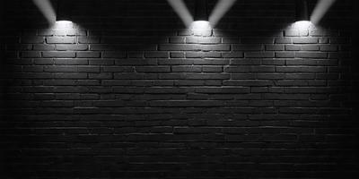 The primary subject of the image is a brick wall with a light shining on it. The setting is a dark room, and the visual style is a black and white photo. The dominant colors are black and white, and the overall atmosphere is moody and dramatic.