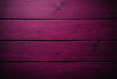 The primary subject of the image is a wooden wall with a purple color. The setting is a room with a wooden floor. The visual style is a close-up of the wooden wall, showcasing its texture and color. The dominant colors are purple and brown, creating a warm and cozy atmosphere.